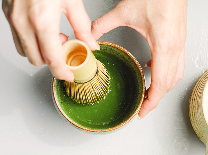 Close-up of vibrant green matcha powder being whisked with bamboo whisk, showing frothy texture and preparation